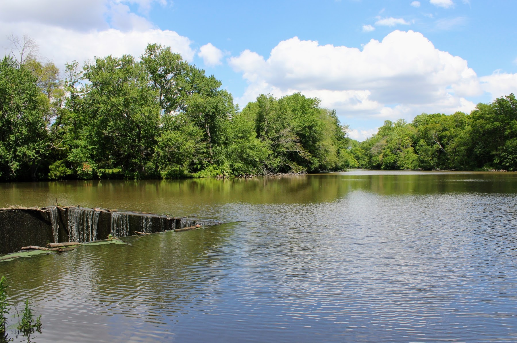 Captures the lake’s water approaching the spillway structure on the western bank, illustrating the scale of the lake before it drops beneath East Lake Road.