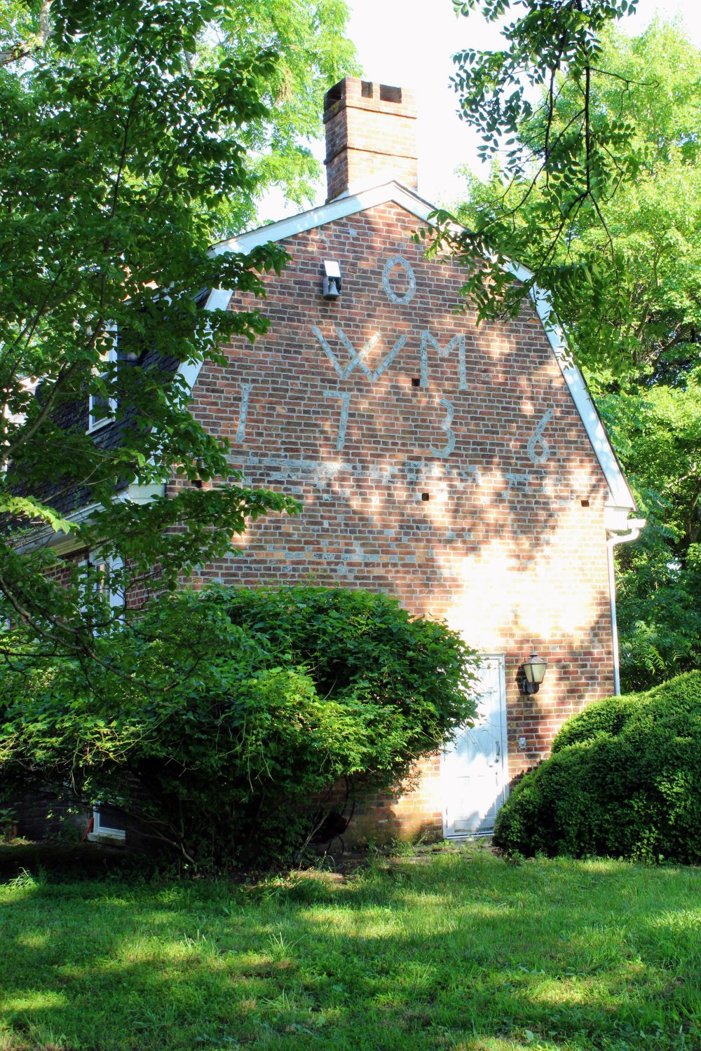 The historic west wall viewed through dappled afternoon sunlight. The shifting shadows demonstrate how the vitrified glazed brick inscription catches the light differently throughout the day.