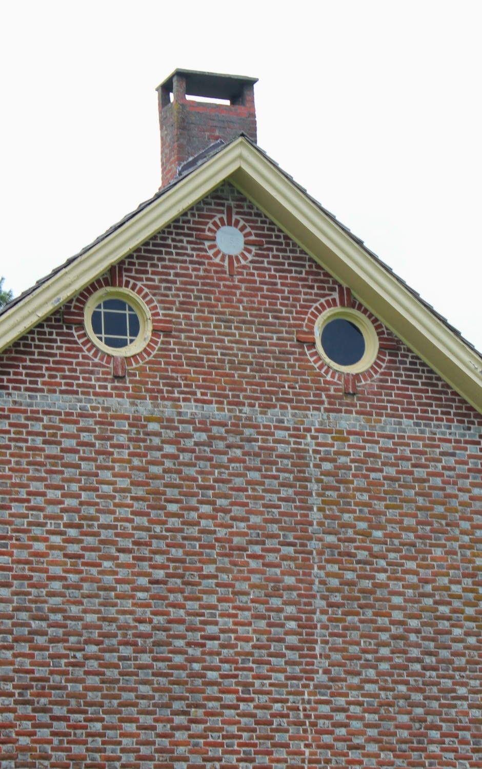 A close-up of the eaves: the two elliptical windows survive intact, but the round marking above them — where a date plate is believed to have once been mounted — has sat empty since at least 1949, when Sickler noted the plate was already lost.