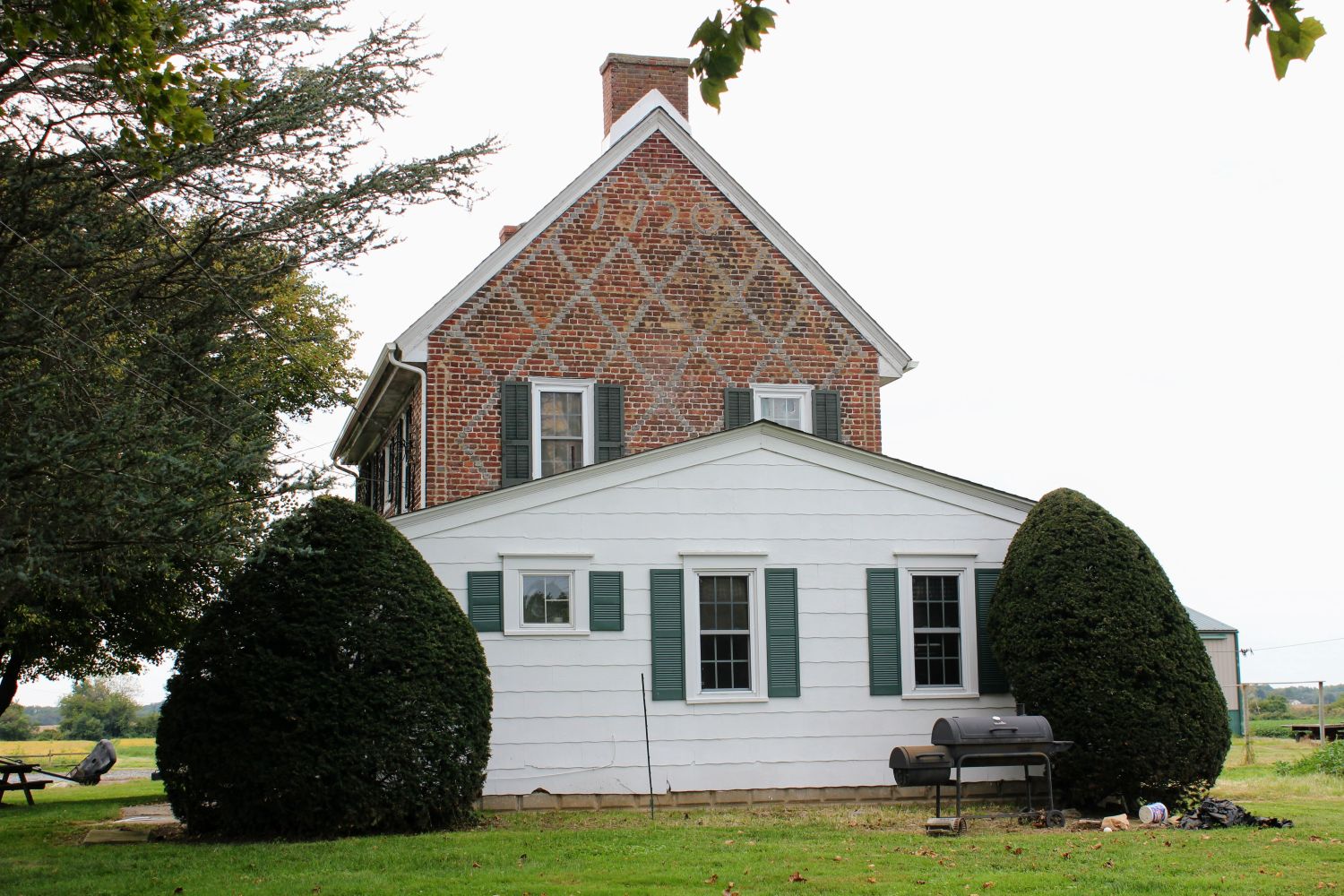 Brick house with white addition in the foreground, red barn visible in the background across an open field.