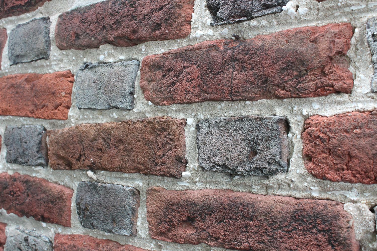 Extreme close-up of a brick wall in a diamond zigzag pattern, alternating dark gray and weathered red brick