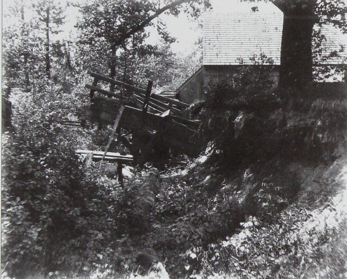 Collapsed timber mill structure tipped into an overgrown gully, an intact shingled gable standing behind it Collapsed timber mill structure tipped into an overgrown gully, an intact shingled gable standing behind it