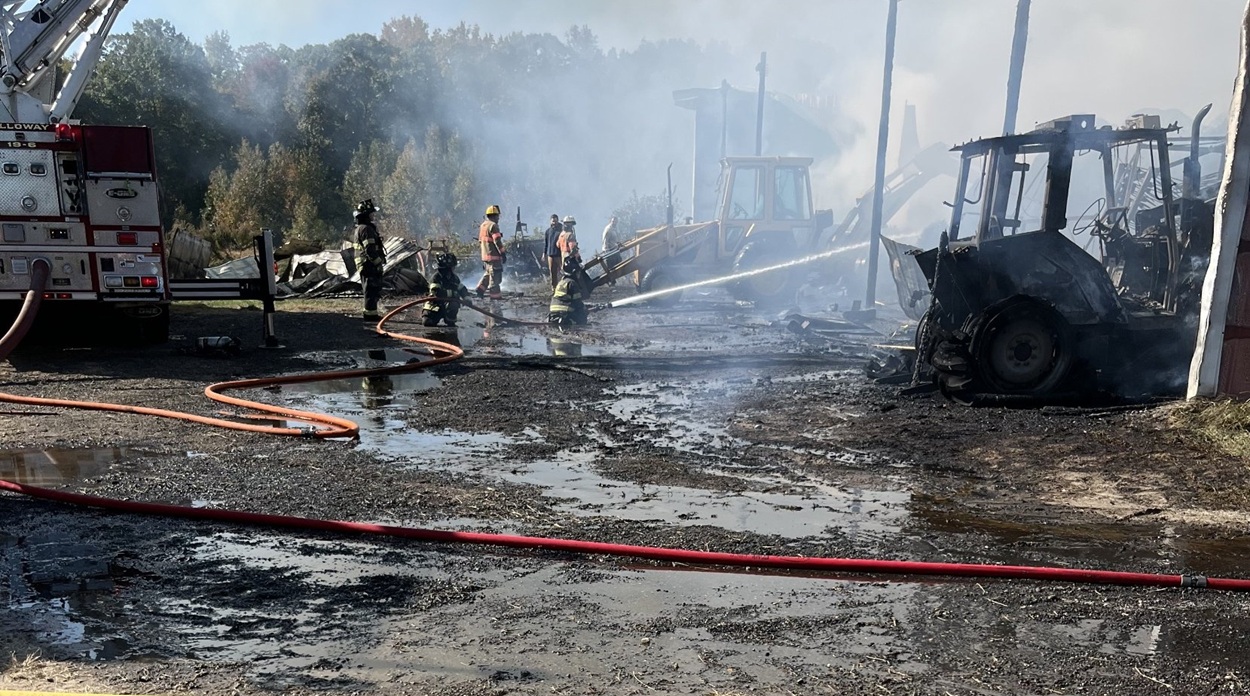 A firefighter directs a hose line near a burned tractor.